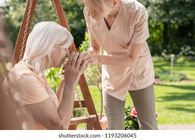 Caregiver Giving Tea To Sick Senior Woman While Relaxing In The Garden