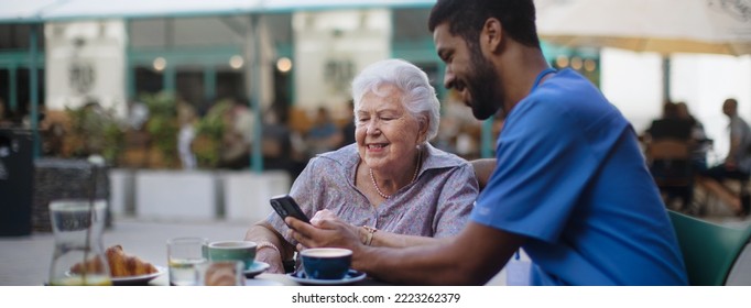 Caregiver having coffee with his client and learning her using smartphone, outdoor at cafe. - Powered by Shutterstock