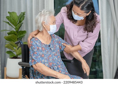 Caregiver Help Asian Senior Or Elderly Old Lady Woman Sitting On Wheelchair And Wearing A Face Mask For Protect Safety Infection Covid 19 Coronavirus.