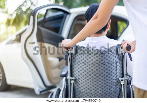 Caregiver helping senior handicapped asian woman from\
wheelchair get into\
car