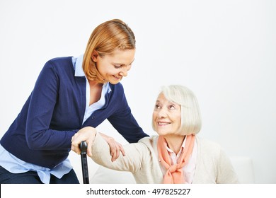 Caregiver Helping Senior Woman With Cane Getting Up From A Sofa