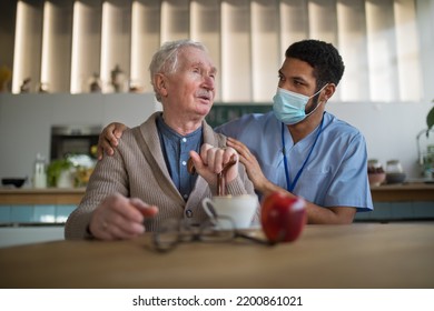 Caregiver With Medical Mask Bringing Healthy Snack To Senior Man In Nursing Home Care Center.