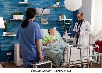 Caregiver Nurse Man Writing Medication Treatment On Clipboard Discussing Healthcare Assistance. Senior Woman Resting In Bed During Social Services Nursing Elderly Retired Female. Support Assistance