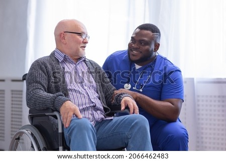 Caregiver and old man in a wheelchair. Professional nurse and patient in a nursing home. Assistance, rehabilitation and health care.