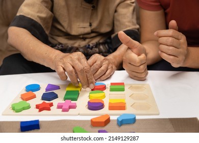 Caregiver And Senior Woman Playing Wooden Shape Puzzles Game For Dementia Prevention