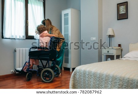 Caregiver with elderly patient in a wheelchair in front of window