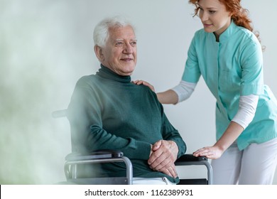 Caregiver supporting happy disabled senior man in a wheelchair in the hospital