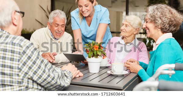 Caregiver with tablet pc and a group of seniors in\
retirement home