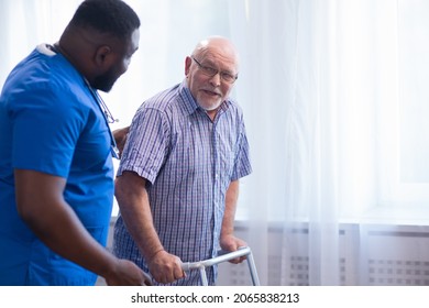 Caregiver is teaching old man to walk with walker. Professional nurse and patient in a nursing home. Assistance, rehabilitation and health.