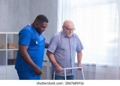Caregiver is teaching old man to walk with walker. Professional nurse and patient in a nursing home. Assistance, rehabilitation and health. - Shutterstock ID 2067685916
