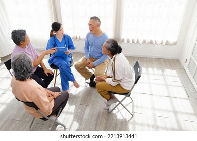 The Caregiver Therapist Sits With A Group Of Asian Senior People In A Circle For Checking Physical And Mental Health In A Group Elderly Therapy Session. The Nursing Home Facilitates A Support Group