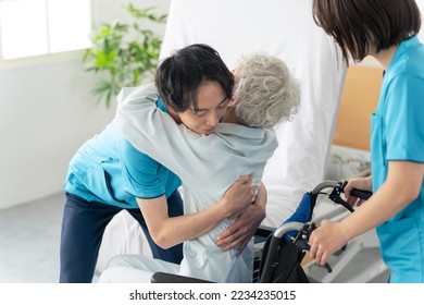 A caregiver transferring an elderly person from a nursing bed to a wheelchair. - Powered by Shutterstock