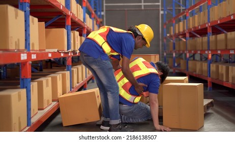 Careless Asian warehouse worker lifting a heavy cardboard box to the shelf then some of the box falling and hit by accident and his friend run to safe or help him. Safety instruction in working area. - Shutterstock ID 2186138507