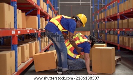 Careless Asian warehouse worker lifting a heavy cardboard box to the shelf then some of the box falling and hit by accident and his friend run to safe or help him. Safety instruction in working area.