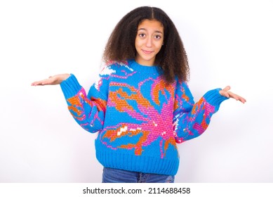 Careless attractive beautiful teenager girl wearing colorful sweater over white background shrugging shoulders, oops.
