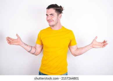 Careless attractive Young caucasian man wearing yellow t-shirt over white background shrugging shoulders, oops.