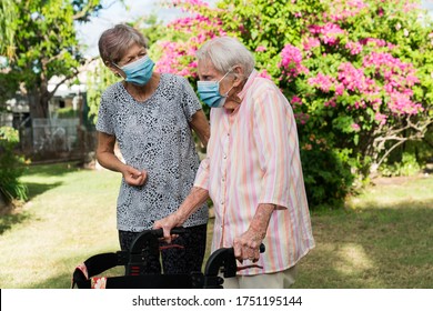 Carer Helping Elderly Lady To Get Exercise In Garden Wearing Mask