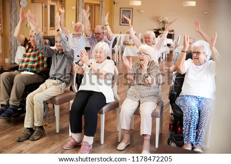 Carer Leading Group Of Seniors In Fitness Class In Retirement Home