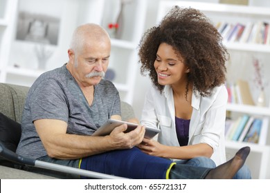 carer and senior man with tablet sitting on the sofa