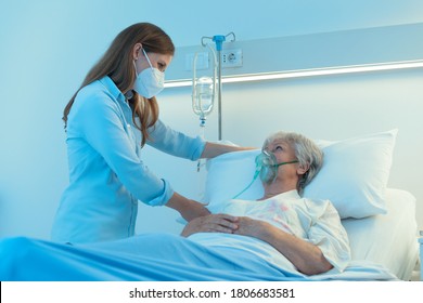 Carer or young daughter wearing a surgical mask checking on a senior female patient wearing a positive pressure oxygen mask to aid breathing in a hospital bed during the Covid-19 pandemic - Powered by Shutterstock