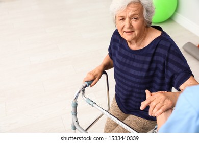 Caretaker Helping Elderly Woman With Walking Frame Indoors