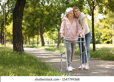 Caretaker helping elderly woman with walking frame outdoors