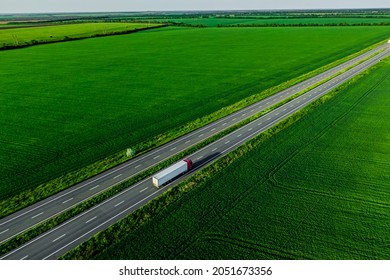 Cargo Delivery. White Truck With Red Cockpit Driving On Asphalt Road Along The Green Fields. Seen From The Air. Aerial View Landscape. Drone Photography. 