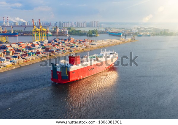 Cargo red ship\
for the transport of cars and other new transport sails from the\
port to the sea, evening\
sunset.