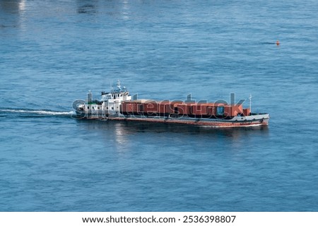 A cargo ship with containers sails under a bridge.