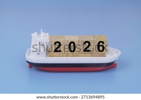 Cargo ship model with cubes with numbers 2026 on blue background. Sea ​​transportation in year 2026 concept.