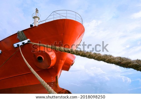 Cargo Ship moored at port with mooring Rope against white clouds on blue sky background