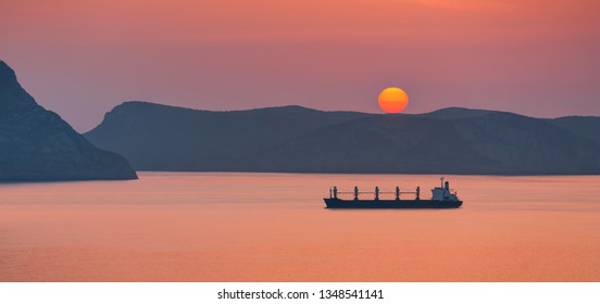 Cargo Ship Sailing Away Against Orange Sunset