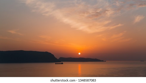 Cargo Ship Sailing Away Against Orange Sunset