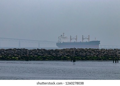 Cargo Ship Sailing Away Under Bridge On Hazy Day