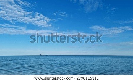 Cargo ship sailing on distant sea horizon under blue sky with scattered clouds. Seascape photography with open water and copy space