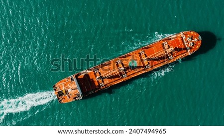 Cargo ship sails on sea. Red boat in middle of green-blue surface of river ocean water sails to port to hand over or pick up commodity, illuminated with bright sun. Aerial above top drone view.