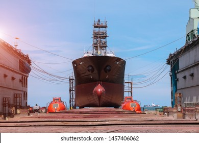 Cargo ship under repair with scaffolding moored on boat sleeper wood for sandblasting and painting at floating dry dock in shipyard Thailand both safety lifeboat moored at side.