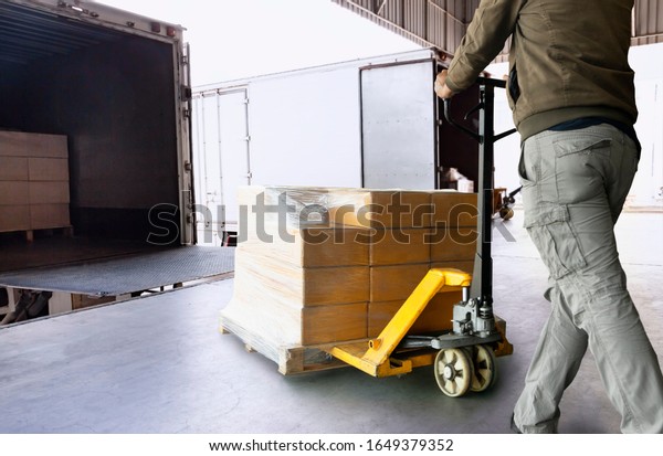Cargo\
shipment loading for truck. Worker courier unloading cargo pallet\
shipment goods, package box, his using hand pallet  jack load into\
a truck, Road freight truck transportation.\
