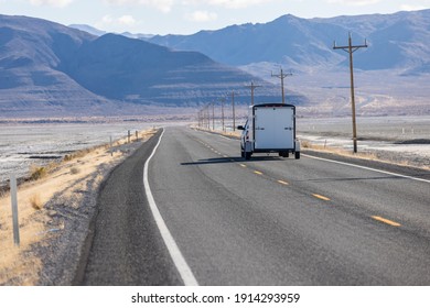 Cargo trailer being pulled down an empty highway stretching for miles into the desert