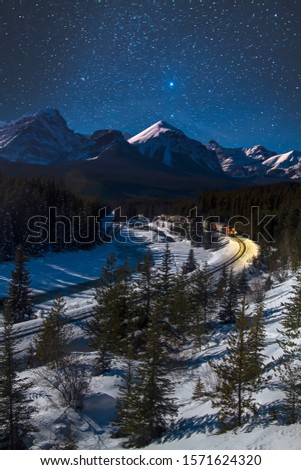 Cargo train making its way through Bow Valley at Morant's Curve during a starry winter night. Banff National Park, Alberta, Canada, Canadian Rockies. Blue winter tones, cold, freezing transportation.
