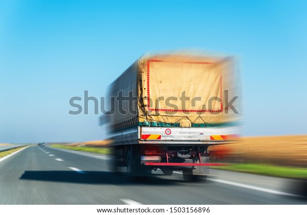 Cargo transportation concept.Fast\
driving lorry  in countryside landscape.Highway view with clear\
blue sky.Truck with container.Blur\
effect.