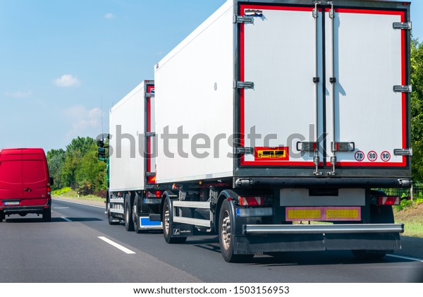 Cargo transportation concept.Fast driving lorry \
in countryside landscape in sunny day.Highway view with blue\
sky.Truck with white\
trailer.