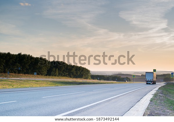 a cargo truck goes\
down a gray highway with a beautiful sunset in the sky and\
beautiful clouds in summer