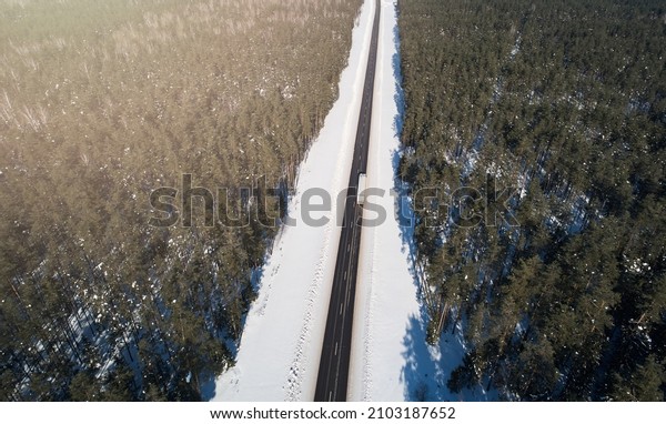 Cargo truck moving on highway road around snowy\
forest aerial above top\
view