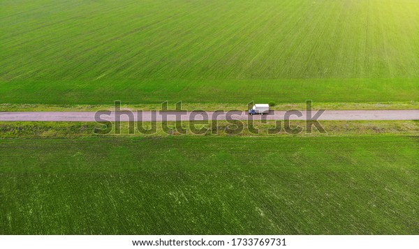 Cargo van driving between the green fields.\
Aerial. View above.