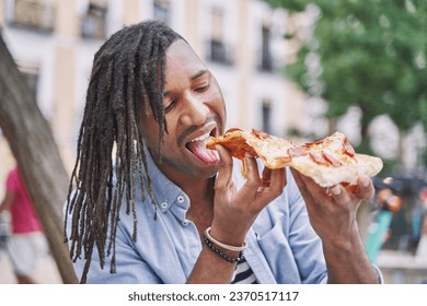Caribbean man with dreadlocks eating a slice of pizza on the street. fast food concept - Powered by Shutterstock