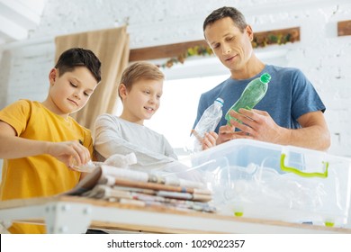 Caring about nature. Charming young man and his pre-teen sons preparing plastic bottles for recycling, crushing the bottles and putting them into special containers - Powered by Shutterstock