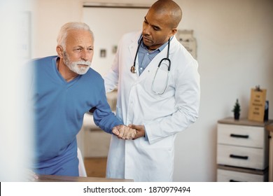 Caring African American Doctor Helping Senior Man To Get Up From His Chair At Nursing Home. Copy Space.