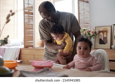 Caring African American Father Helping His Twin Babies To Take Seat In High Chairs To Have Lunch At Home