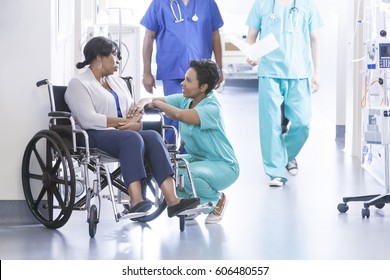 Caring African American Female Nurse In Hospital Uniform Scrubs With Wheelchair Patient In Medical Centre